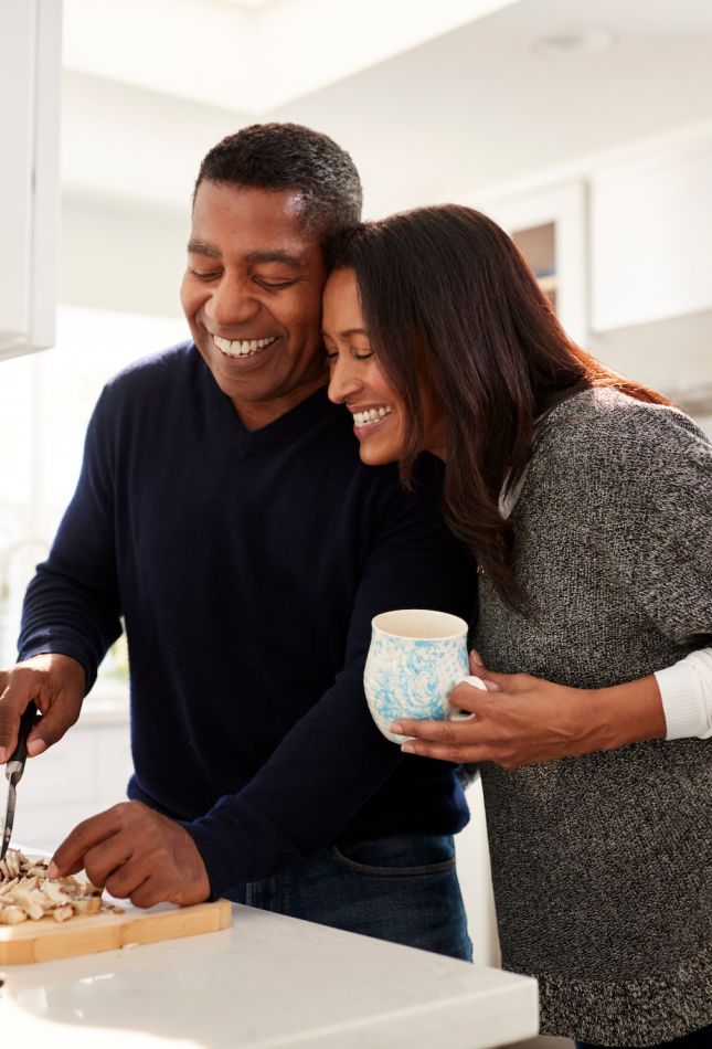 Middle aged mixed race couple standing at worktop in the kitchen preparing food following a recipe on a tablet computer, selective focus