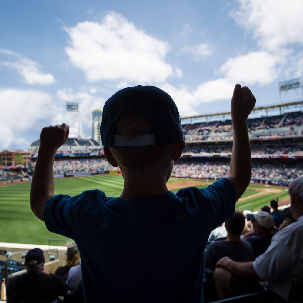 Little boy standing up in baseball stands raising his hands during a baseball game
