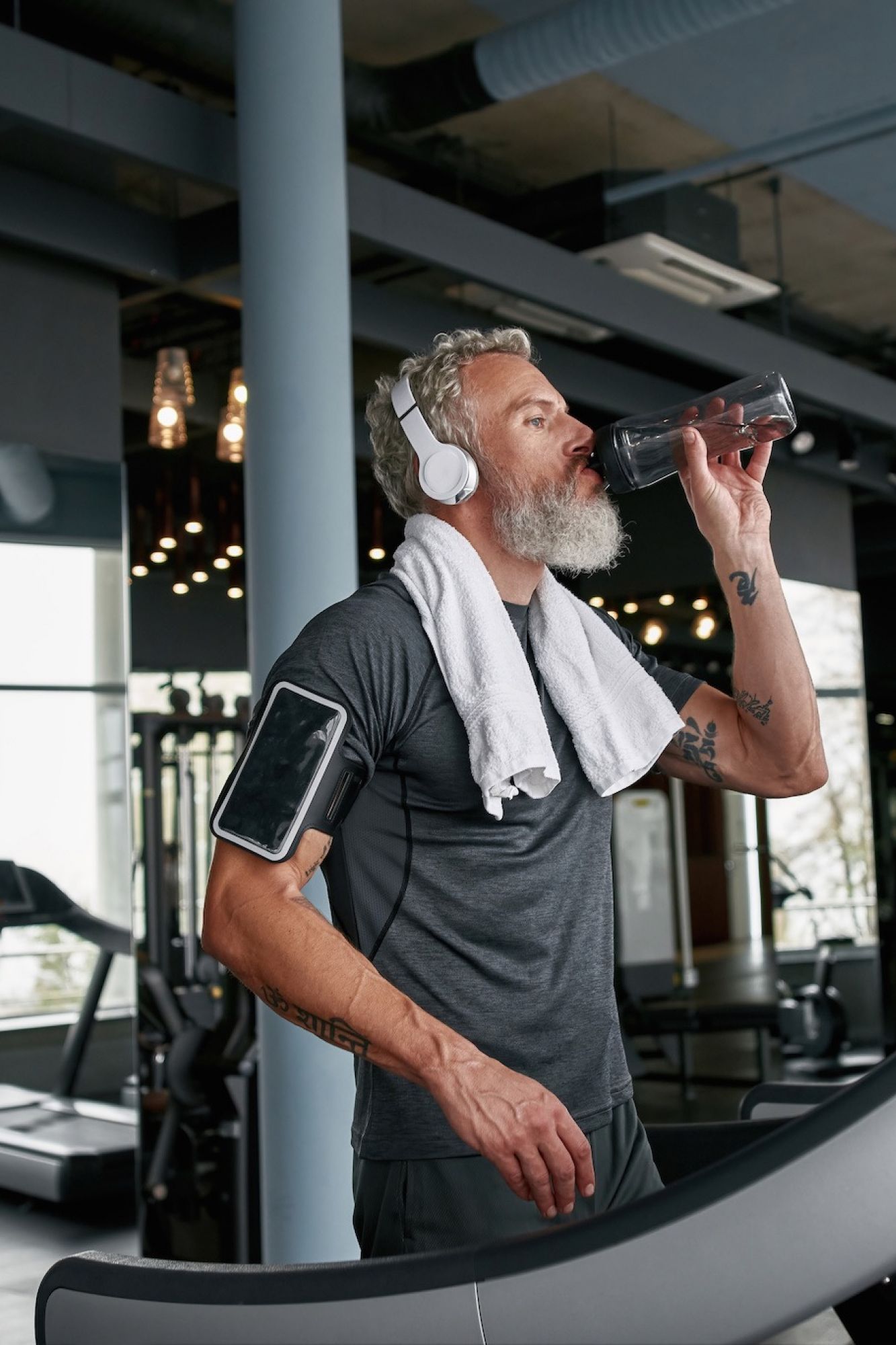 Senior man walking on treadmill in apartment gym taking a sip of water