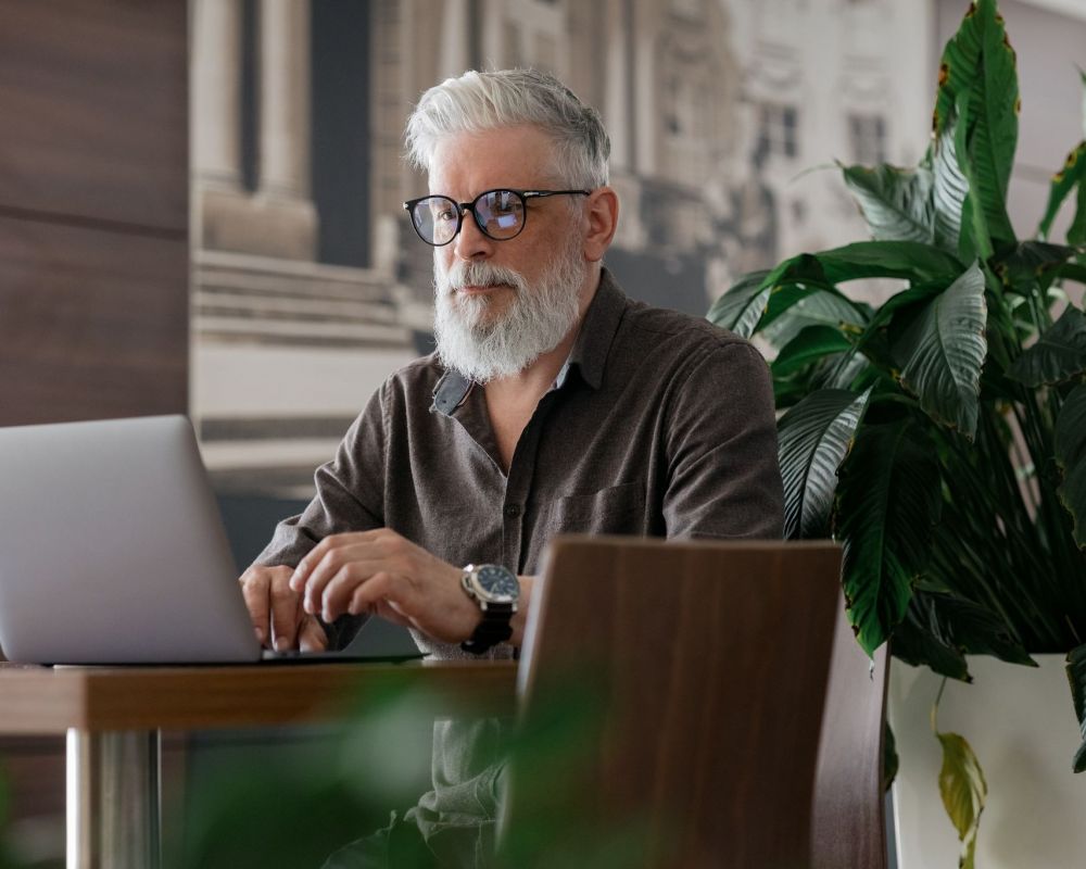 Senior man using laptop while sitting at table with house plant behind
