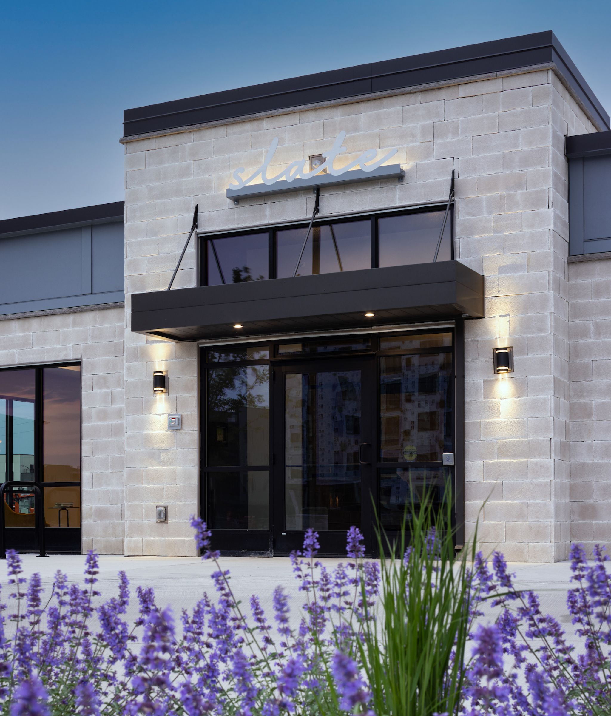 Slate exterior view to front door with beautiful white brick building bordered by lavender plants.