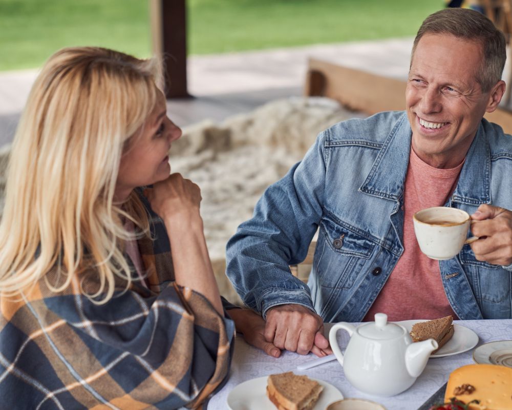 Senior couple smiling at each other over coffee on their private apartment patio