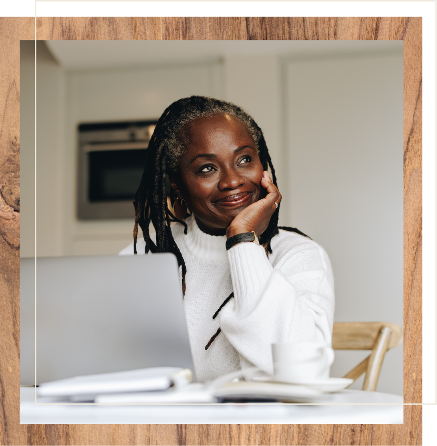 Black senior woman smiling while sitting at table and working on laptop
